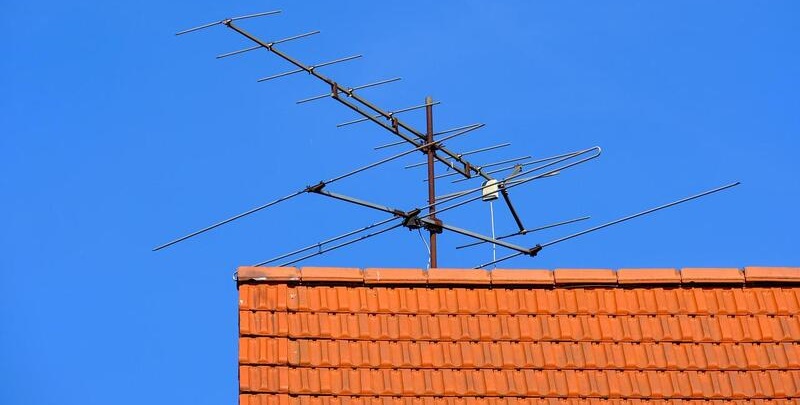 Television antenna on red tiled roof in clear blue sky