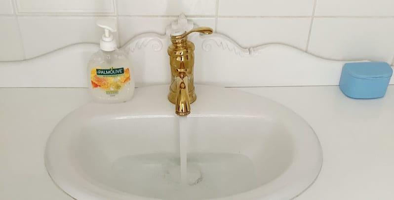 Gold or brass tap with water flowing into a white bathroom sink.