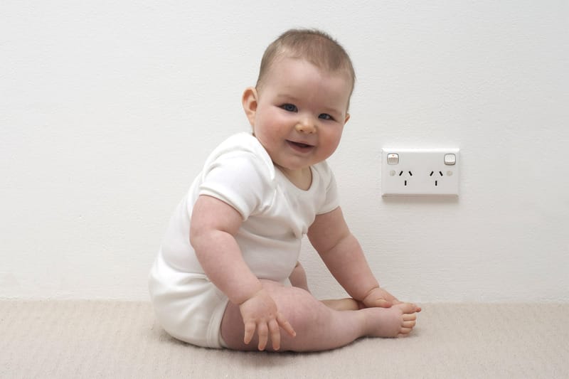 young toddler sitting next to an electrical outlet